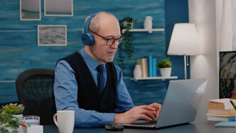 Konzentrierter-Alter-Unternehmer-Mit-Kopfhörern,-Der-Musik-Hört-Und-Auf-Dem-Laptop-Tippt