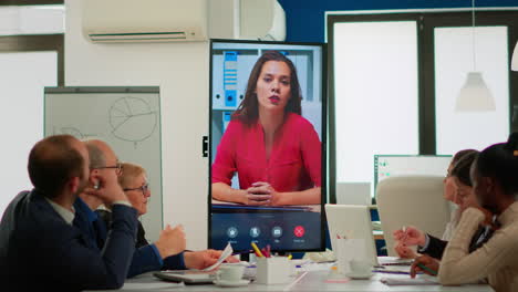 Diverse-executive-team-meeting-at-conference-video-call-looking-at-huge-display