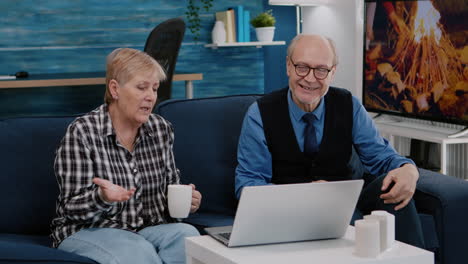 Enthusiastic-couple-of-pensioners-sitting-together-on-sofa-talking-on-video-call