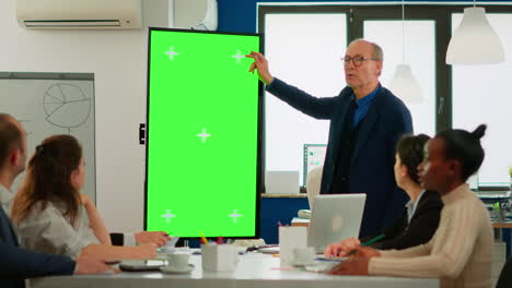 Mature-businessman-analysing-reports-standing-in-conference-room-pointing-at-green-screen-monitor
