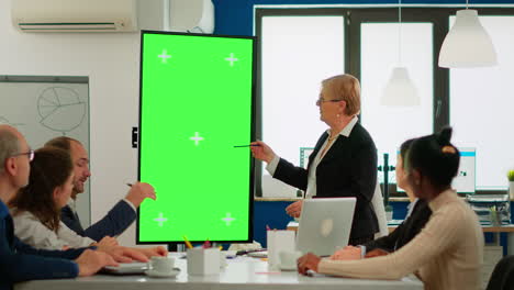 Team-leader-standing-at-meeting-table-analysing-financial-statistics,-looking-at-green-screen-display