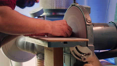 Manufacturer-shaping-wooden-bowl-on-disc-sander-in-assembling-shop