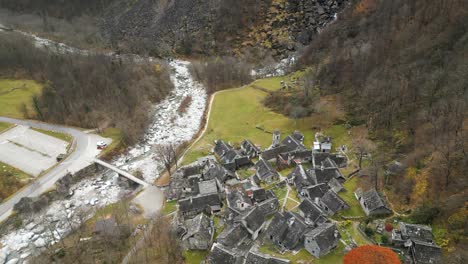 Aerial-drone-top-down-shot-over-village-houses-alongside-river-Maggia-in-Cavergno,-district-of-Vallemaggia-in-the-canton-of-Ticino,-Switzerland-on-a-cloudy-day