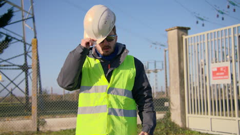 Male-engineer-closing-his-jacket-with-zipper-and-wears-hard-hat-safety-helmet-at-the-electric-substation-handheld-dynamic