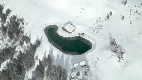 Aerial-drone-top-down-shot-over-partly-frozen-lake-beside-chairlift-in-Engelberg-Brunni-bahnen,-Switzerland-on-a-sunny-day