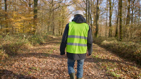 Male-engineer-walking-alone-in-the-forest-while-carrying-clipboard-to-survey-for-trees,-handheld-following