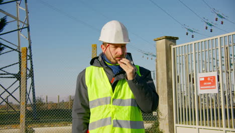 Male-engineer-wearing-sunglasses-on-his-safety-reflective-vest-while-standing-at-the-electric-substation,-handheld-dynamic