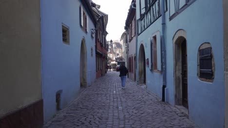 Female-tourist-walking-in-the-historical-streets-of-the-medieval-city-with-gobblestone-roads-in-Colmar,-France