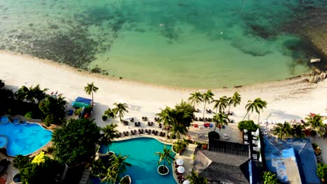 Drone-tilting-upwards-showing-the-buildings-of-a-resort-in-Thongson-Bay,-the-fine-sandy-beachfront,-and-the-crystal-clear-waters-of-the-Gulf-of-Thailand,-in-Koh-Samui-island-in-Surat-Thani-province
