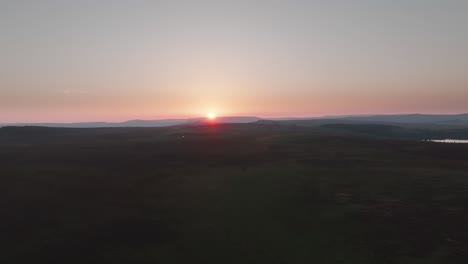 Sunset-over-expansive-moorland-on-hazy-summer-day,-aerial-drone