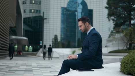 Businessman-working-sitting-on-the-bench-outside-an-office-building