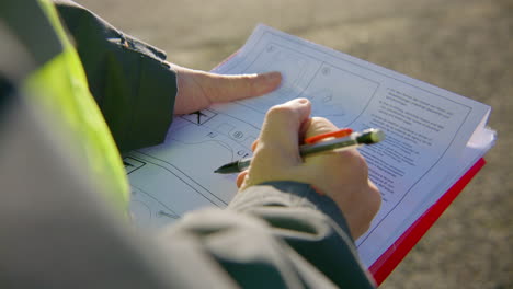 Engineer-reading-and-analyzing-schematics-on-the-clipboard-while-holding-a-pen,-handheld-closeup
