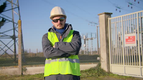 Male-engineer-wearing-safety-reflective-vest-and-sunglasses-while-crossing-his-arms-at-the-electric-substation,-handheld-dynamic