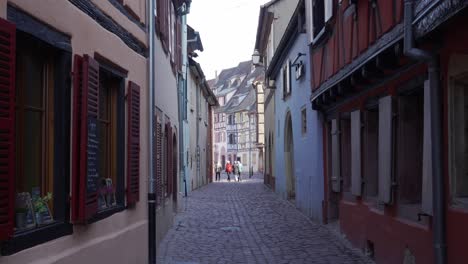 People-walking-through-the-small-gobblestone-streets-of-medieval-town-in-Colmar,-France,-with-half-timbered-houses
