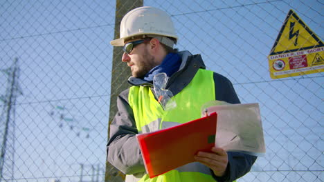 Male-engineer-holding-clipboard-and-dictating-instructions-while-pointing-directions,-handheld-dynamic