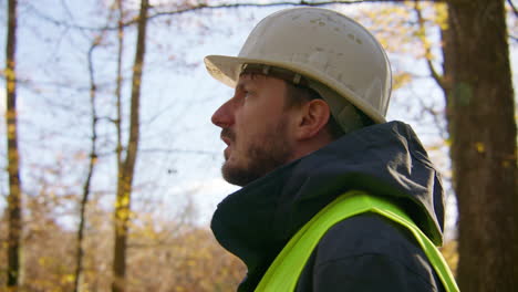 Closeup-shot-of-the-face-of-a-worker-wearing-hard-hat-and-safety-vest-in-the-middle-of-the-forest,-handheld