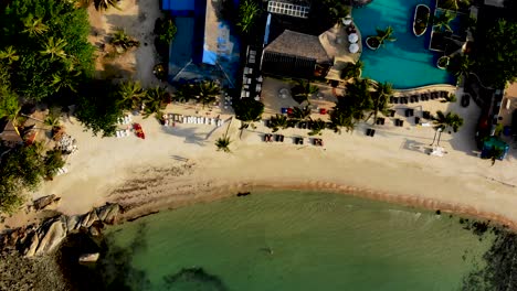 Overhead-drone-shot-moving-down-towards-the-beachfront-of-Thongson-Bay-where-beachgoers-are-swimming-and-sunbathing-in-front-of-one-of-the-secluded-resorts-in-Koh-Samui-island,-Thailand
