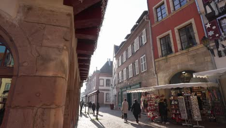 Beautiful-morning-sun-shining-through-the-streets-of-medieval-town-in-France-people-walking-around-shop-area