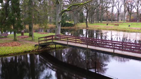 Wooden-bridge-in-park-over-a-pond-in-late-autumn-on-a-gloomy-day