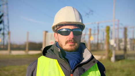 Male-engineer-wearing-safety-reflective-vest-and-sunglasses-while-standing-at-the-electric-substation,-handheld-closeup
