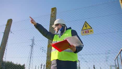 Male-engineer-holding-clipboard-and-pointing-directions-while-dictating-instructions,-handheld-dynamic