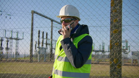 Male-engineer-listening-over-the-walkIe-talkie-while-nodding-his-head-at-the-electric-substation,-handheld-closeup