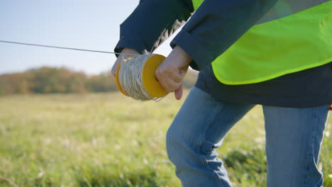 Male-engineer-deploying-a-wire-across-the-grassy-field-from-handheld-spool-of-cable-on-a-rod