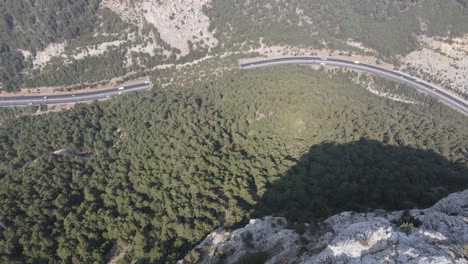 Highway-traffic-passing-through-the-mountains,-tunnel-view-taken-from-the-cliff-with-a-drone
