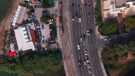 Top-down-aerial-shot-of-a-tram-driving-along-side-a-busy-road