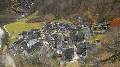 Aerial-drone-rotating-shot-over-river-Maggia-flowing-alongsidevillage-houses-in-Cavergno,-district-of-Vallemaggia-in-the-canton-of-Ticino,-Switzerland-at-daytime