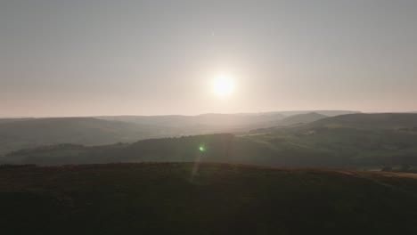 Drone-flight-over-rolling-hills,-low-sun,-hazy-summer-day,-countryside