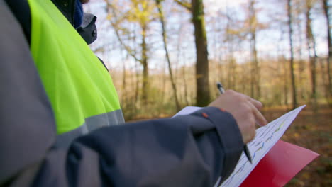 Closeup-shot-of-the-worker-while-taking-notes-on-his-document-at-the-clipboard-in-the-middle-of-the-forest,-handheld