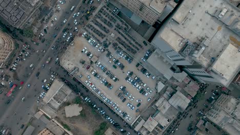 Vogelperspektive-Auf-Einen-überfüllten-Parkplatz-Und-Eine-Stark-Befahrene-Straße-Zwischen-Gebäuden-Und-Belebten-Straßen,-Saddar-Karachi,-Pakistan
