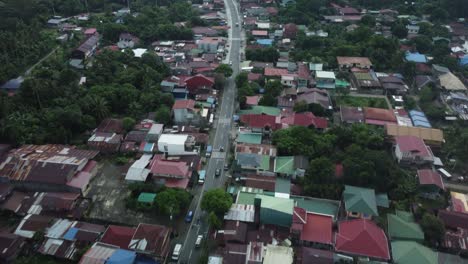 Drone-shot-of-Provincial-Philippine-highway,-with-cars-moving,-surrounded-by-trees-and-small-houses