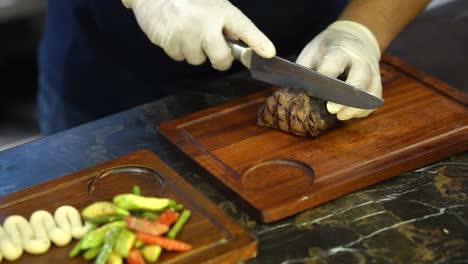 Up-close-chef-with-gloves-cutting-juicy-piece-of-beef-steak-with-sharp-knife