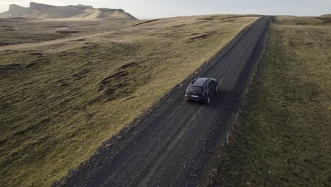 Aerial-cinematic-establisher-black-car-drives-in-dramatic-landscape,-Iceland
