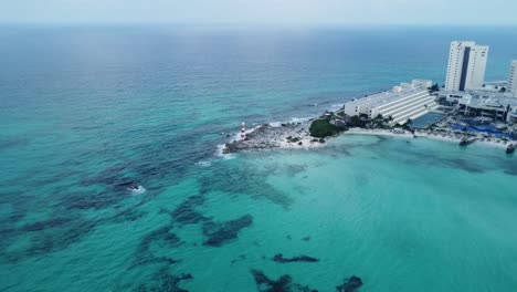 Aerial-of-the-Punta-Cancun-Lighthouse,-an-iconic-structure-in-Cancun-Mexico,-standing-as-a-sentinel,-commanding-panoramic-views-of-the-turquoise-waters-that-stretch-out-to-the-horizon