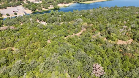 Moving-quickly-above-a-large-section-of-trees-that-gives-way-to-a-tiny-cabin-campsite-near-a-lake-inlet-that-has-a-boat-ramp-and-recreational-shoreline-and-space