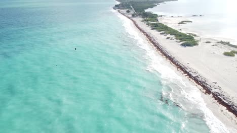 Isla-Blanca-from-the-sky,-the-aerial-perspective-reveals-a-charming-tableau-where-gentle-waves-caress-the-pristine-white-sand-beach