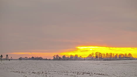 Time-lapse-frozen-field-close-to-road,-moving-clouds-golden-sky-rural-Riga,-Latvia