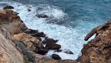 Sea-waves-loosing-their-power-and-crashing-into-rocks-at-the-beach,-captured-during-daytime,-untouched-nature-concept
