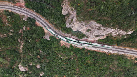 Top-down-drone-shot-showcasing-two-trains-elegantly-passing-each-other-along-a-verdant-and-lush-cliffside,-all-under-the-tranquility-of-an-overcast-day