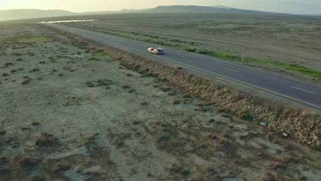 The-drone-camera-is-moving-from-front-to-back,-where-the-car-is-going,-and-the-mountains-are-visible-behind-it