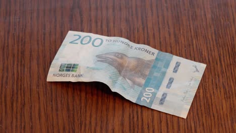 Hand-Placing-Norwegian-200-kr-Note-in-center-of-Wooden-Table