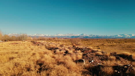 Drone-Avanzando-Sobre-El-Desierto-De-Malargüe,-Con-La-Imponente-Cordillera-De-Los-Andes-Nevada-Al-Fondo