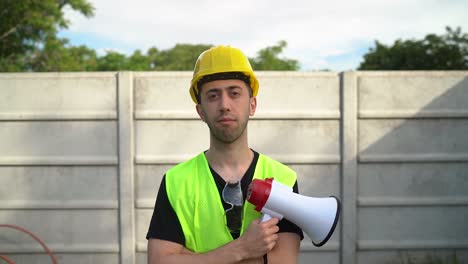 A-Construction-Worker,-Clad-in-a-Yellow-Hard-Hat-with-Standard-Safety-Spectacles-Hanging-From-the-Neckline-of-His-Shirt,-is-Gripping-a-Megaphone---Medium-Close-Up