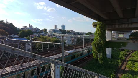 Zug,-Der-Unter-Einer-Brücke-Mit-Hanggebäuden-Im-Hintergrund-In-Tokio,-Japan,-Hindurchfährt