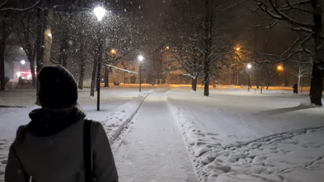 Women-walking-alone-at-night-on-snow-path-in-urban-park-of-Riga,-Latvia