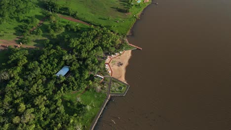 Drohnenaufnahme-Aus-Der-Luft,-Die-Einen-Freizeitort-Entlang-Des-Paraná-Flusses-Einfängt-Und-Einen-Malerischen-Ausflugsort-Am-Flussufer-Mit-Freizeiteinrichtungen-Enthüllt