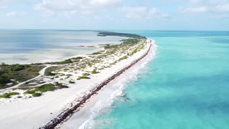 Aerial-of-Isla-Blanca,-Mexico,-the-aerial-view-unveils-a-picturesque-scene-where-waves-gently-crash-onto-the-pristine-white-sand-beach